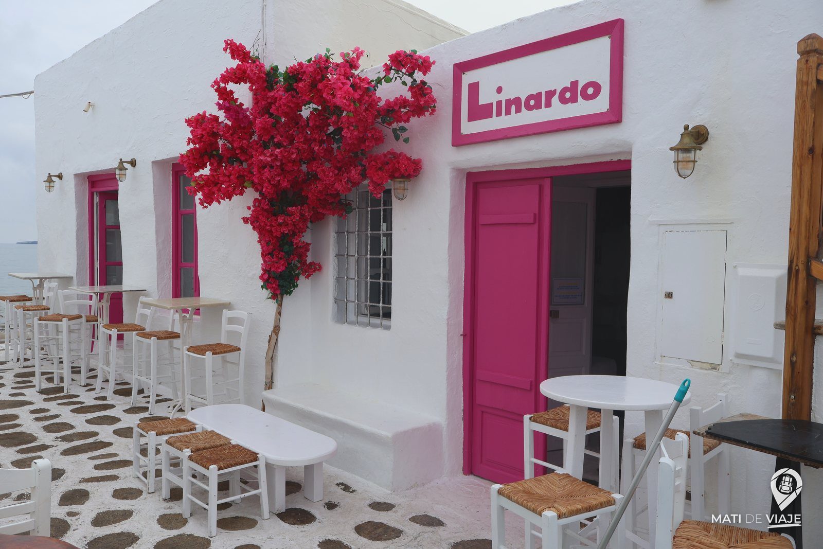 Café blanco con puerta fucsia y buganvilla en Naoussa, Paros